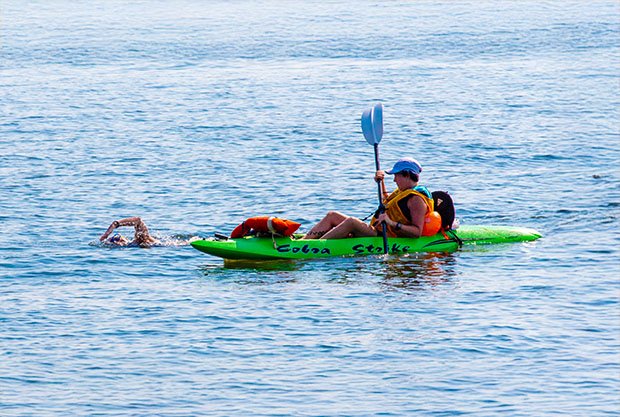 individual-kayaking-alongside-swimmer-calm-water-daylight